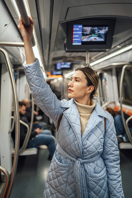 一名女子站在地铁里，手握扶手