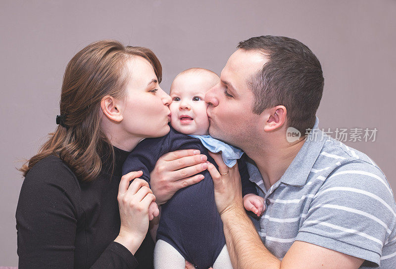 一个年轻的白人家庭的肖像，一个年轻的男人和女人拥抱和亲吻一个小婴儿
