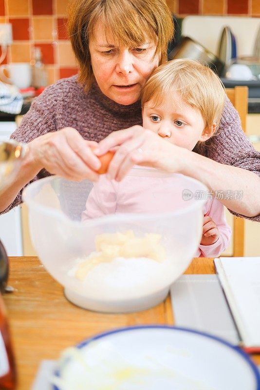 祖母在厨房的桌子上教她的孙子如何打鸡蛋和准备蛋糕混合物