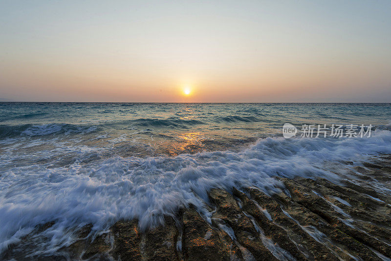 日落时海浪冲击着海岸线上的岩石。罗德岛，希腊