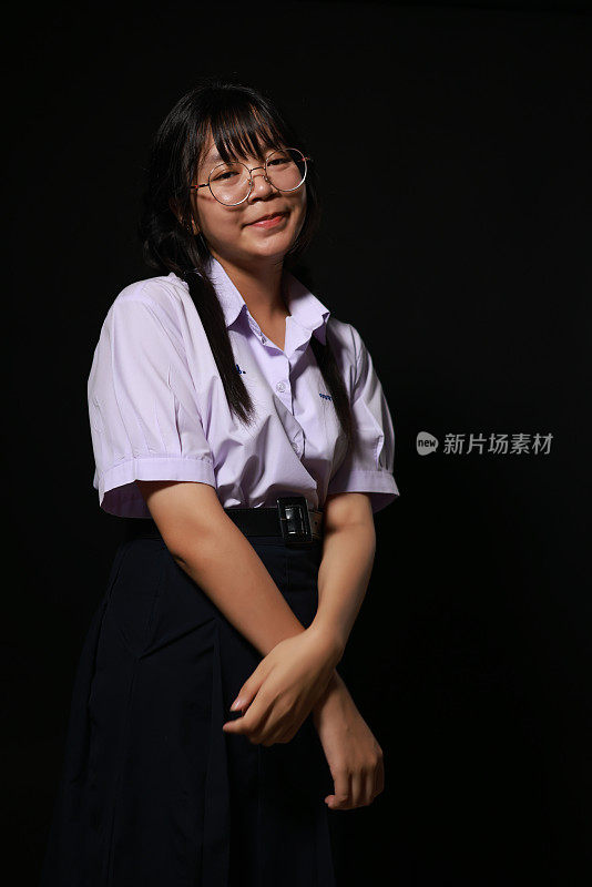 微笑的脸。年轻的亚洲女学生穿着校服，戴着黑色背景的眼镜。女学生肖像，工作室横幅标题。学校孩子的脸，拷贝空间。