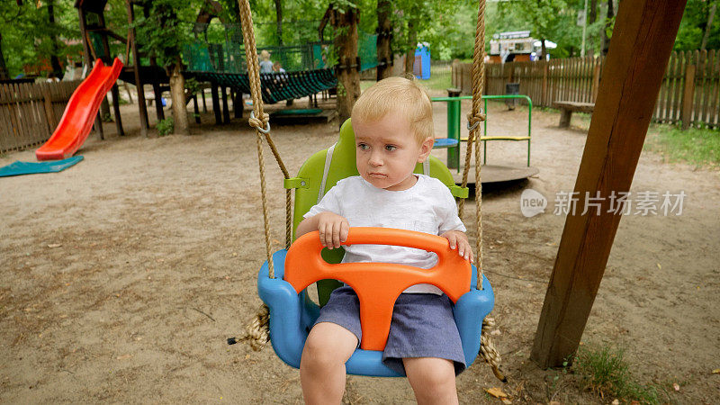 可爱的小男孩坐在公园的彩色秋千上荡秋千的特写。孩子们在户外玩耍，孩子们玩得开心，暑假和假期。