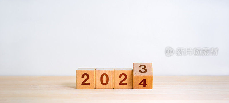 2024年新年快乐，换新时代理念。将2023年至2024年的日历数字翻转在木制立方体块上，隔离在木制桌子和白色横幅背景上，极简简约的风格。