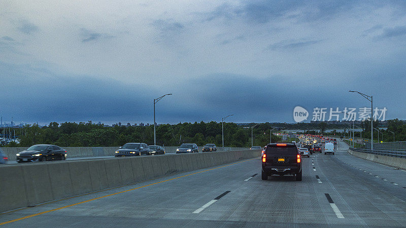 黄昏的公路交通。汽车行驶在纽约布鲁克林的贝尔特公园路上。从车窗看到迎面而来的汽车映衬着暮色的天空。