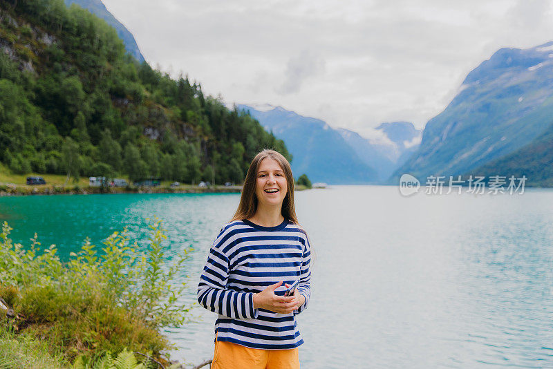 带着智能手机的快乐女旅行者在挪威的湖边思考夏天的户外活动