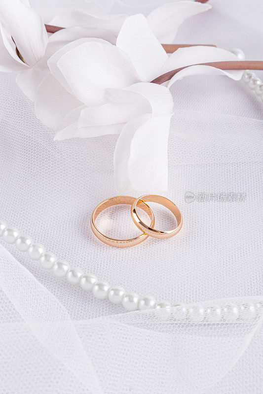 别致的垂直婚礼背景贺卡，邀请，封面设计。精致的白花，两只金婚戒，珍珠串珠。
