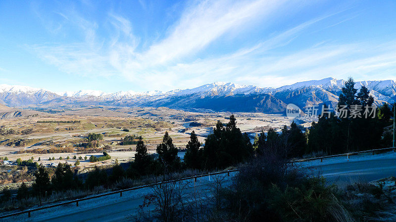 在遥远的新西兰南岛，一条高架的风景公路，远处有冬天的树木和白雪皑皑的山脉