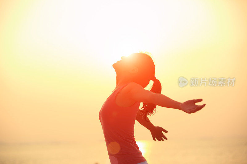 欢呼的女人在日出的海滩上张开双臂