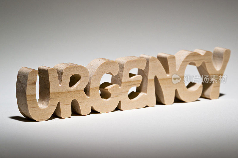 “紧急”这个词刻在木头上的白色背景上。