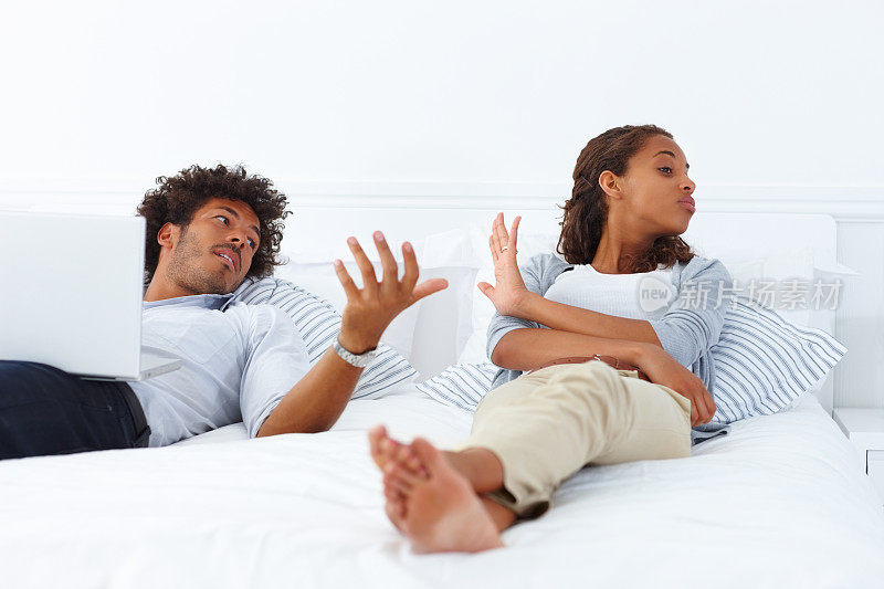 这是一对年轻的非裔美国夫妇躺在床上争吵的照片