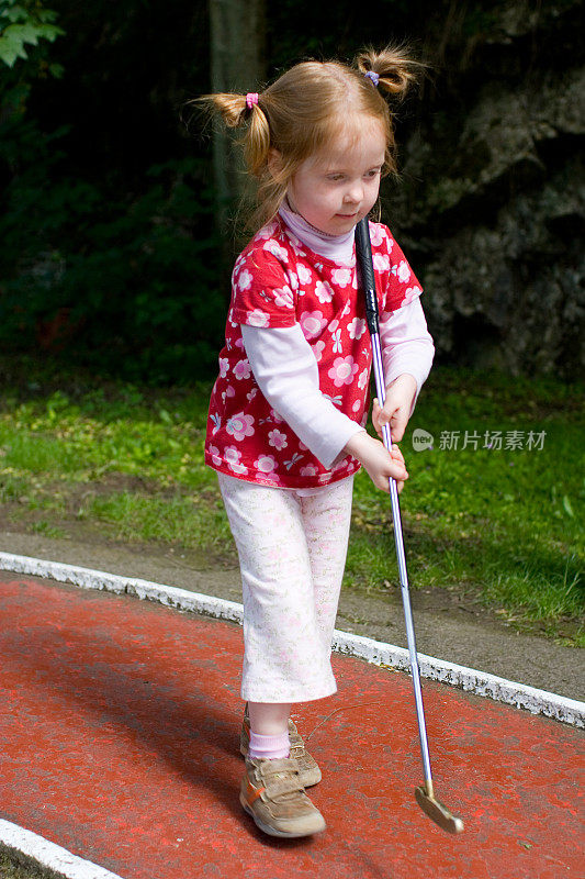 小女孩在全神贯注地打她的第一场迷你高尔夫
