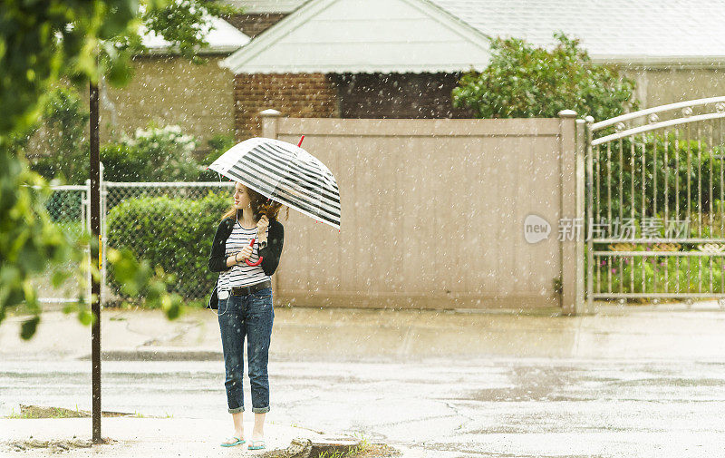 少女撑着伞在雨中走在街上。纽约皇后区