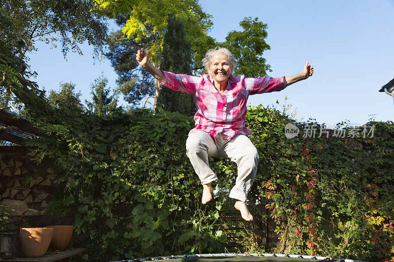 快乐超重的老年妇女在蹦床上跳