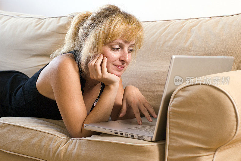 年轻女子躺在沙发上用笔记本电脑