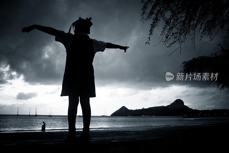 小女孩的侧影手臂伸展在暴风雨的海滩上