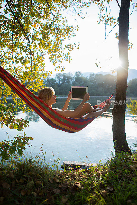 日落时分，一名女子在吊床上用平板电脑拍照