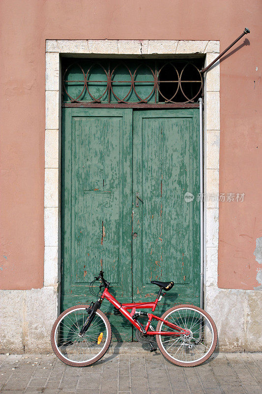 一辆红色的自行车斜靠在一个古老的绿色大门上