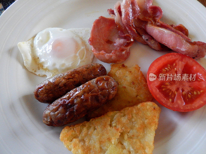 这是一份有香肠、培根、土豆泥和西红柿的油炸早餐
