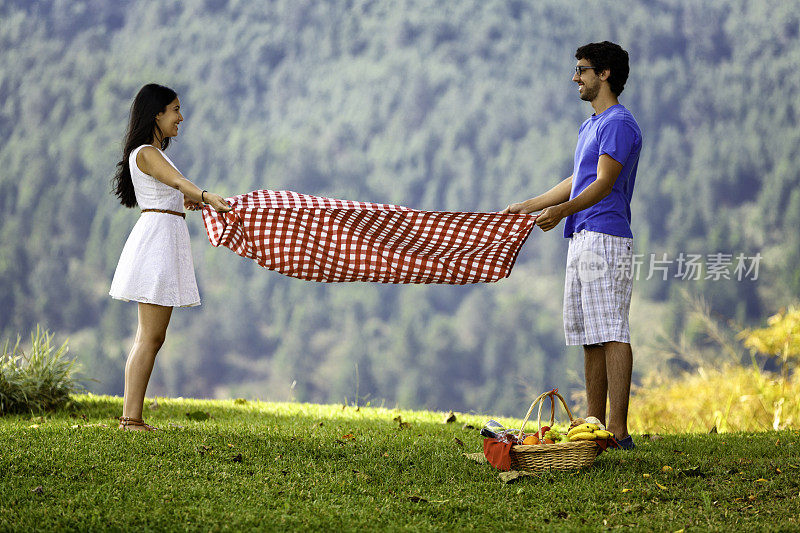 年轻的西班牙或拉丁夫妇在公园设置野餐毯
