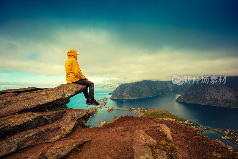 峡湾和渔村全景鸟瞰图。一名游客坐在悬崖峭壁上。美丽的山的风景。挪威自然，罗浮敦群岛。