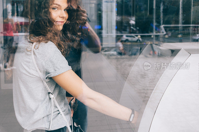 年轻的卷发微笑的女人从一个ATM机取款