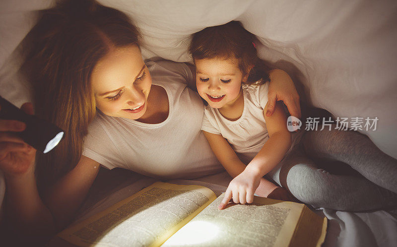 母亲和孩子在毯子下用手电筒看书