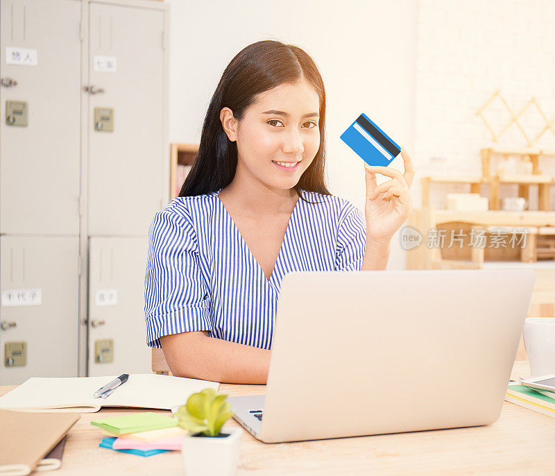 快乐的亚洲女人在网上购买笔记本电脑和支付信用卡在她的家庭办公室