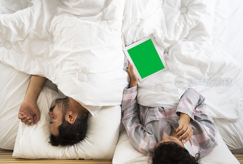 年轻夫妇在床上，女人在用绿色屏幕的数字平板电脑