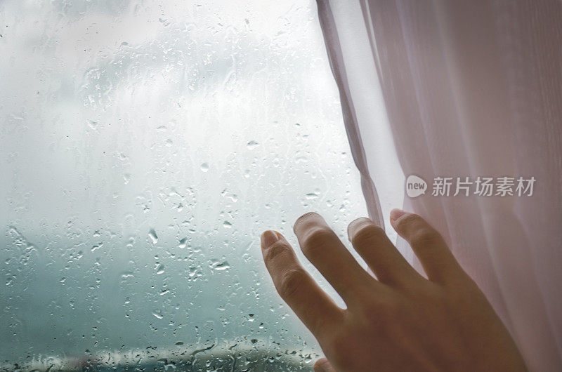雨天——一个女人的手从下雨的窗户拉下百叶窗。