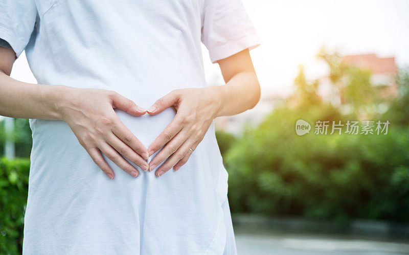 一个孕妇在肚子上摆出心形的姿势