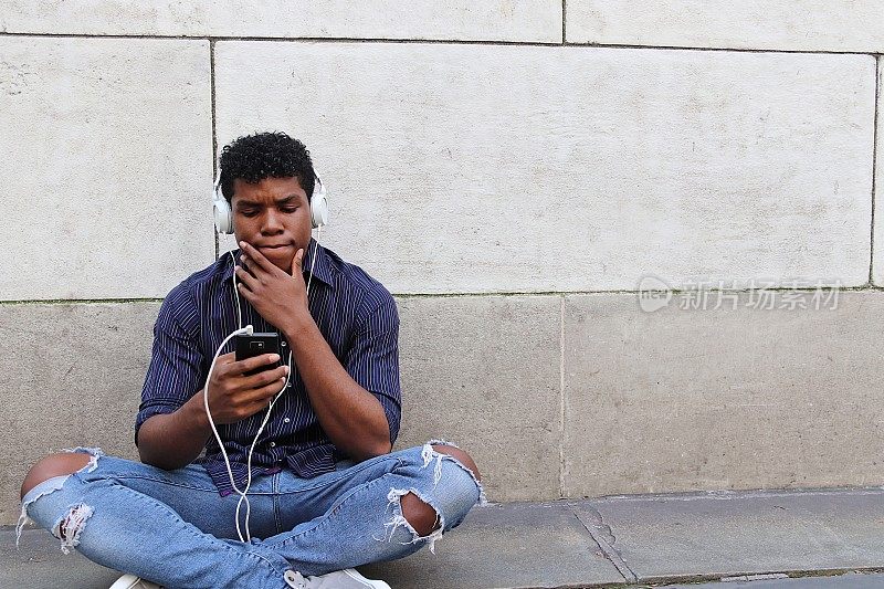 一个年轻人靠着水泥墙坐在外面用普通的手机