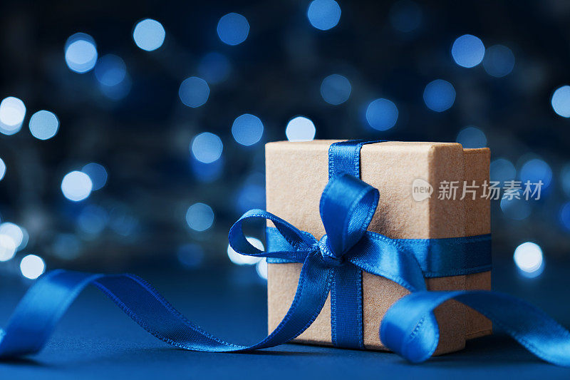 以蓝色散景为背景，配蝴蝶结丝带的节日礼盒或礼品。神奇的圣诞贺卡。