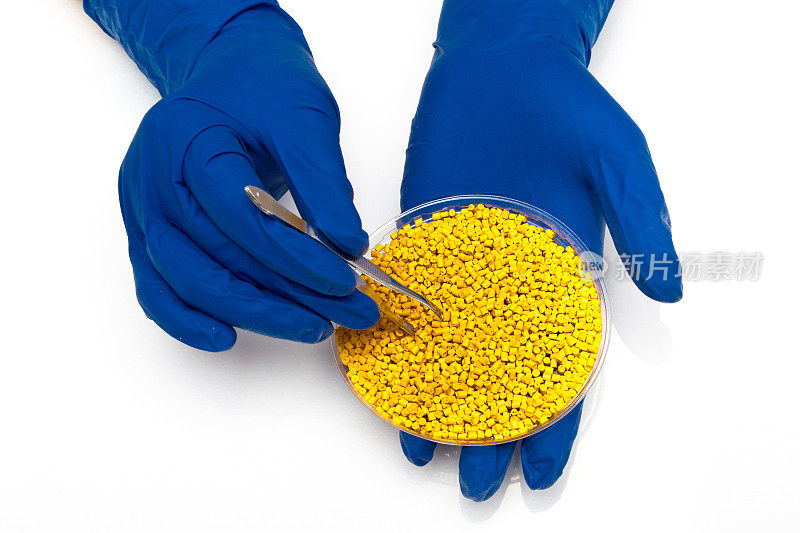 塑料颗粒。颗粒状聚合物的着色剂。手上拿着塑料小球，戴着手套和镊子