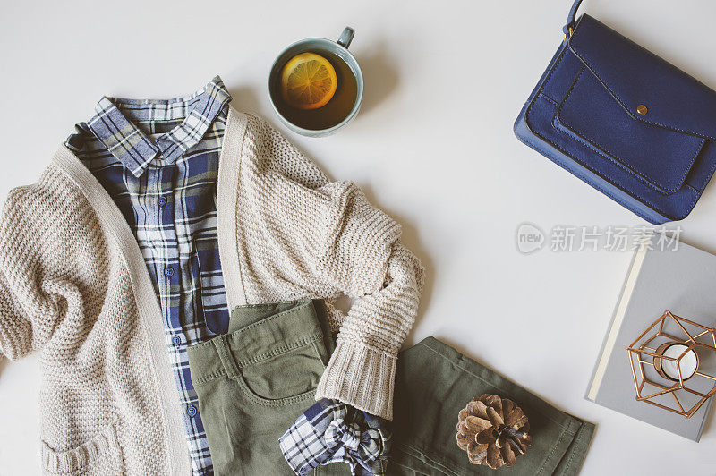 舒适的秋女人休闲装套装，平躺与复制空间。格子衬衫，针织毛衣，蓝色斜挎包和卡其布裤子在白色背景。时尚时尚，俯视图。