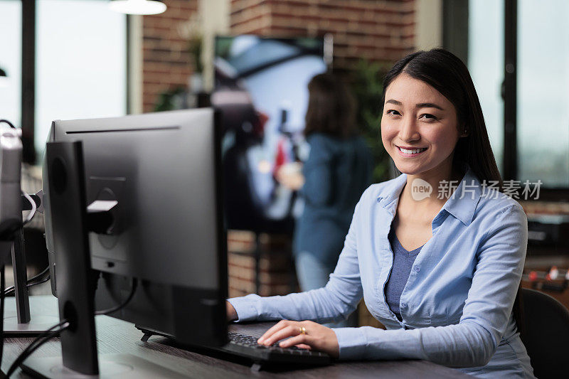 微笑的公司员工坐在办公空间的办公桌前，看着相机。