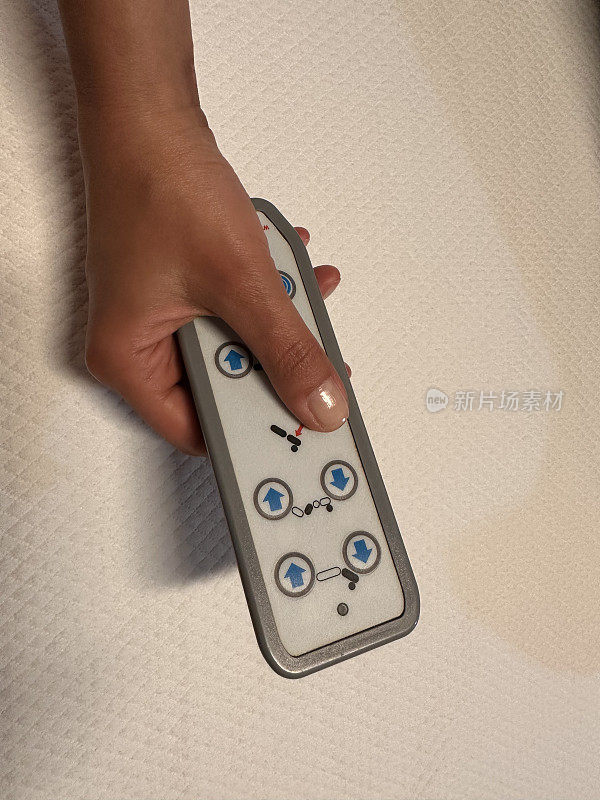 妇女的手按电动可调病床的遥控按钮的特写
