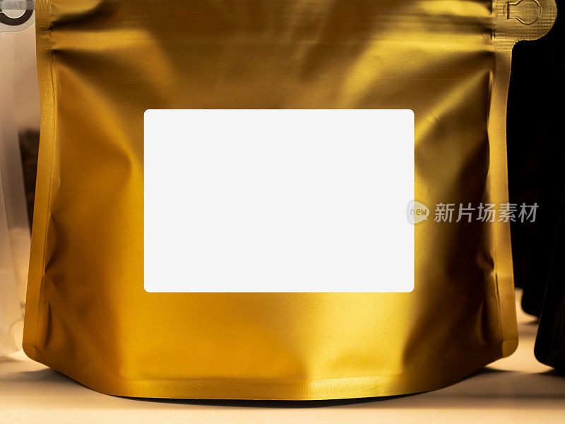 近照:现代咖啡包装上的金箔袋上的空白白色标签。样板贴纸标签。前纸拉链袋包装咖啡豆显示在货架上。