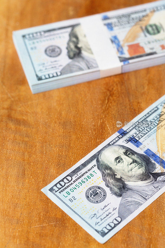 100美元的钞票散落在木质表面上，其中包括一捆用货币带包裹的钞票