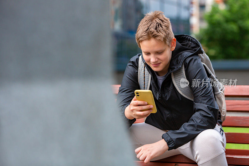 十几岁的小学生背着书包在公园里用手机阅读任务