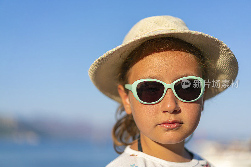 一个戴着帽子和太阳镜的女孩在海滩上的肖像
