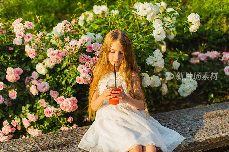 穿白裙子的金发女孩手里拿着水果鸡尾酒。夏天的生活方式。的童年。清凉饮料