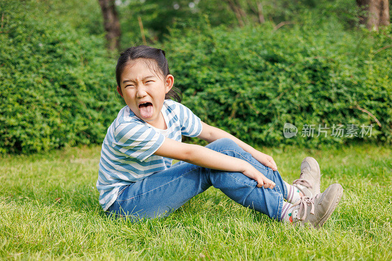 调皮的小女孩坐在草地上做鬼脸