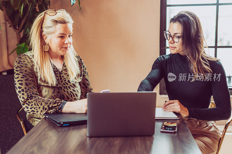 工作中的女性，会议桌旁拿着笔记本电脑的两位女企业家，商业伙伴或客户和代理人
