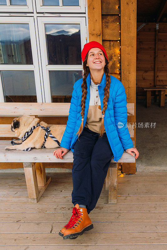 挪威，一个快乐的女人带着一只狗，头戴红帽，在山上欣赏冬天的时光