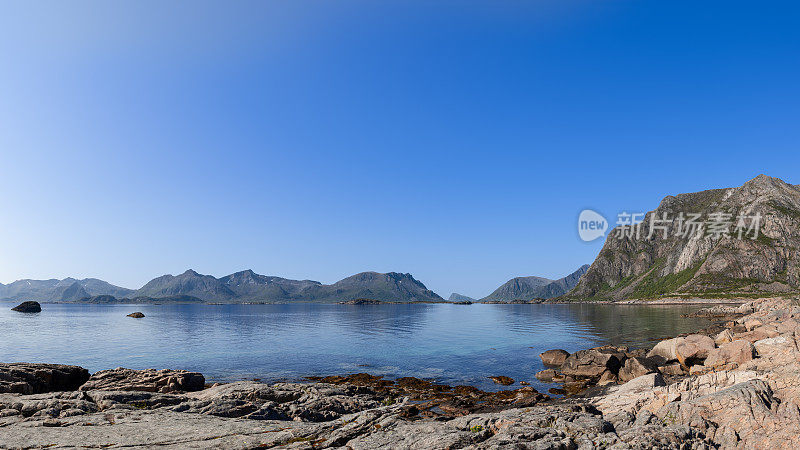 罗弗敦崎岖的海岸线在晴朗的天空下展开，群山耸立在宁静的挪威海后面，是挪威自然风光的原始范例