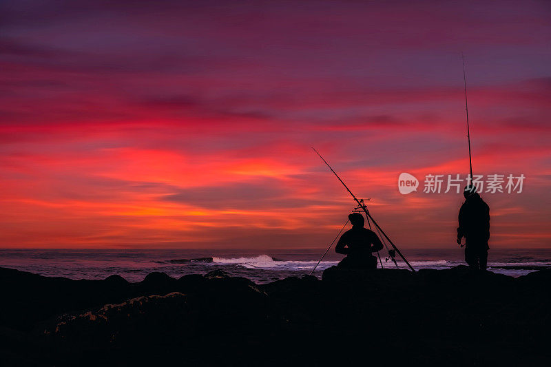 两个人海上钓鱼的剪影与惊人的日落和海上的云景