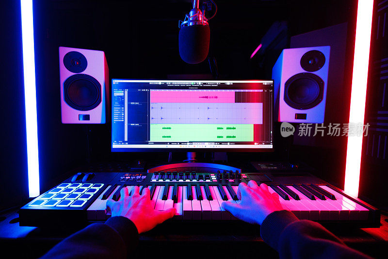 一位男音乐家在录音室里弹奏midi键盘合成器，专注于自己的双手。