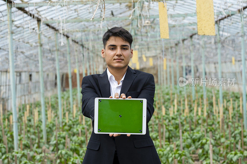 年轻的企业家用他的数码平板电脑控制着温室