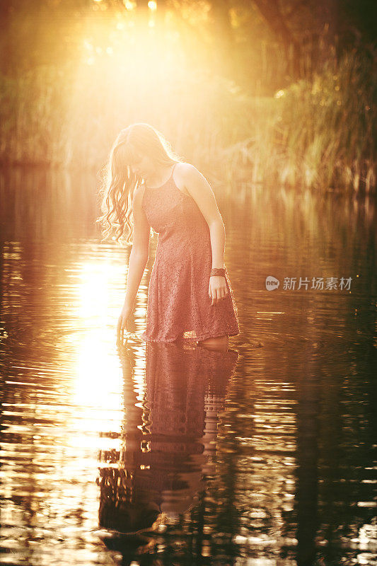 沉思的年轻女子涉水在湖在日落