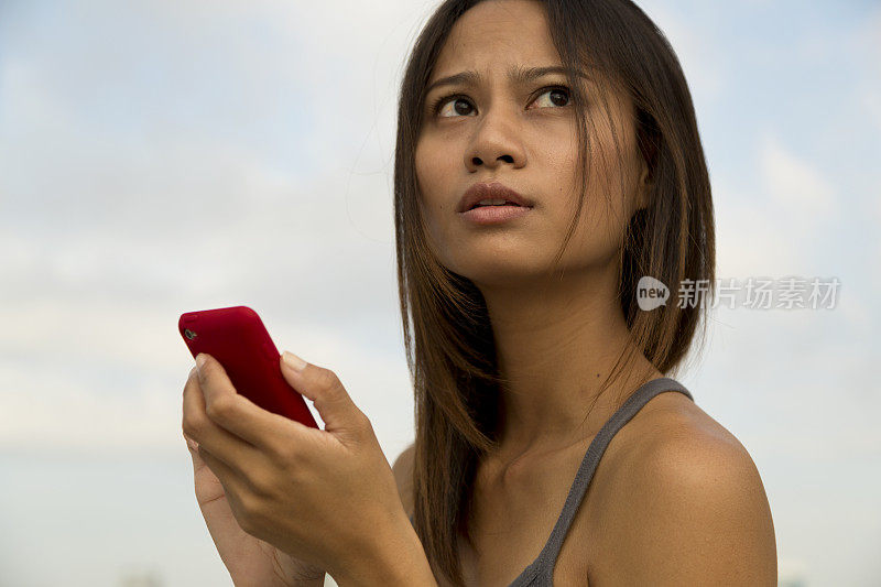 一名年轻的亚洲女子给手机发短信，忧心忡忡